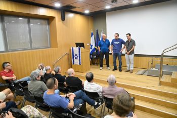 Prof. Avi Zadok delivering a heartfelt speech of appreciation on stage, joined by Barak Filosof and Alon Katz.